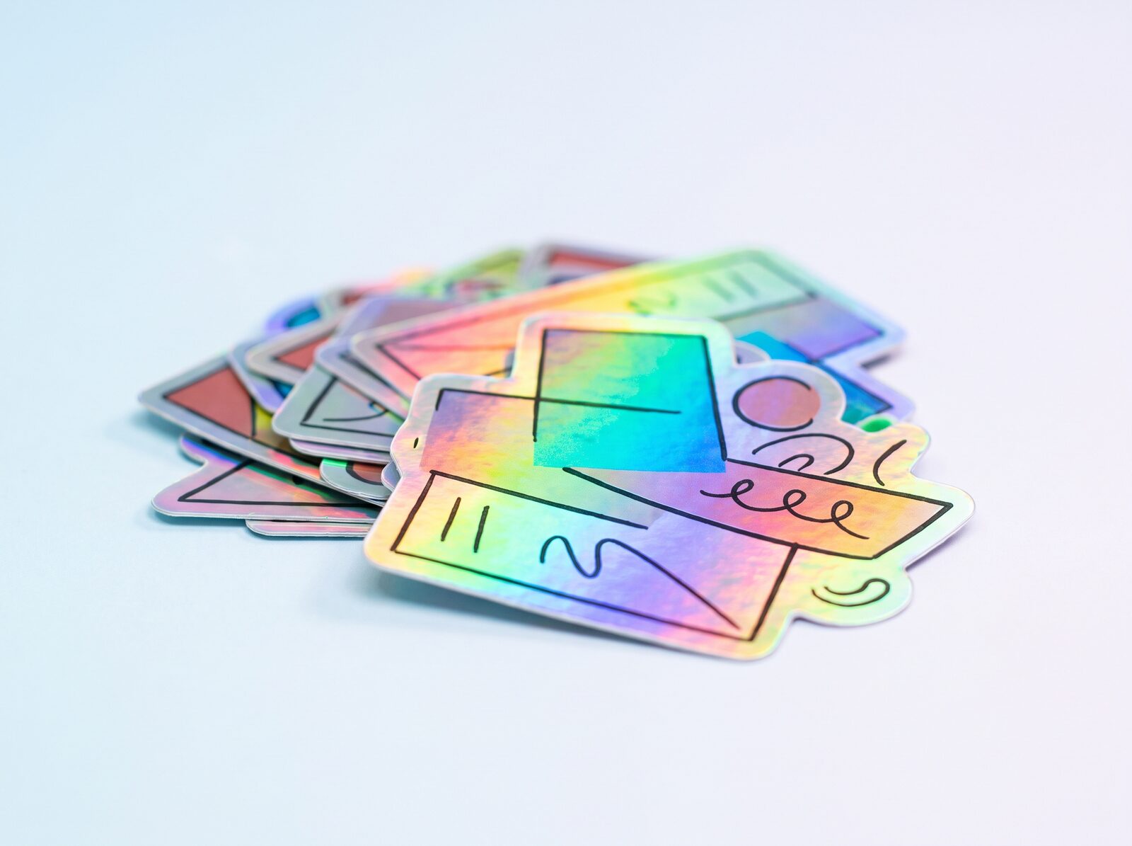 Holographic die-cut laptop stickers in a pile, catching a rainbow shift